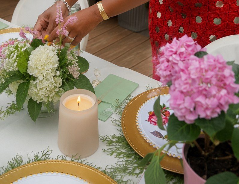 Hands arranging a small bouquet of white hydrangea beside a lit candle on a set table.