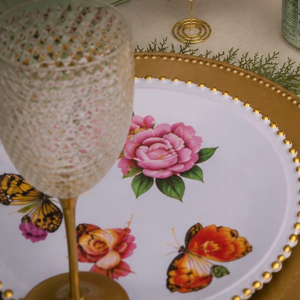 A place setting with a floral plate on a gold charger and a textured glass.