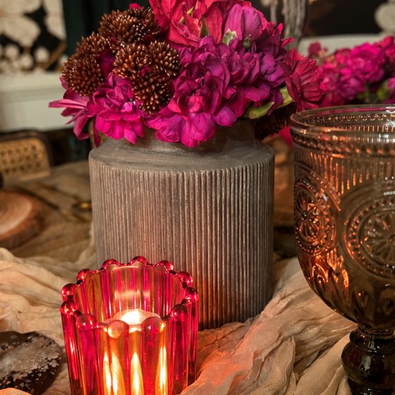 Magenta flowers in a ribbed vase beside a red votive on Toya's table.