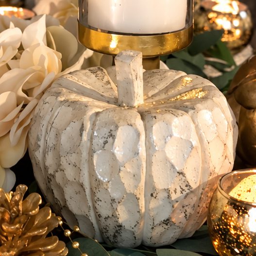 A white pumpkin and a pillar candle in a gold rimmed glass on Vee's table.